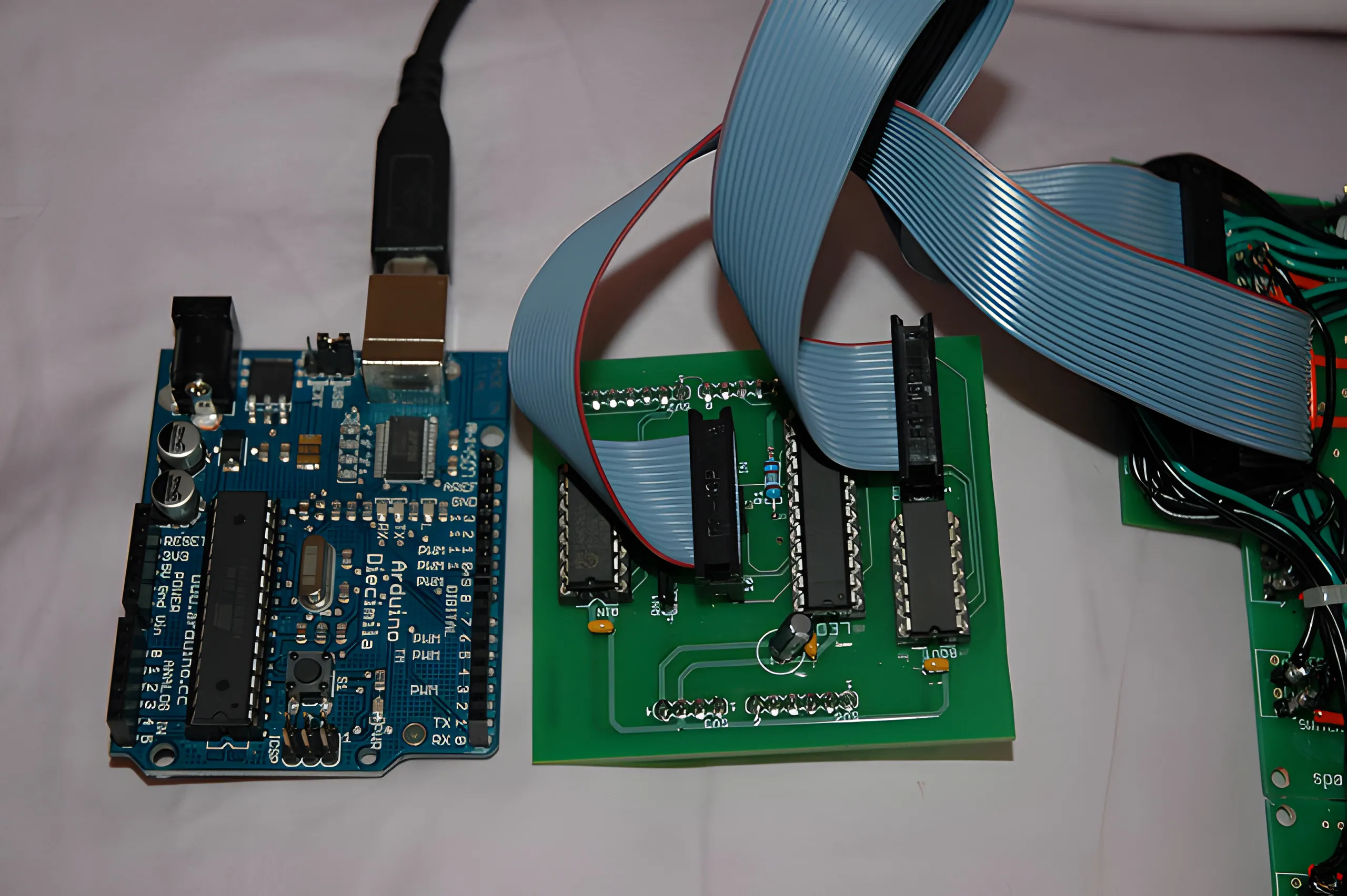 Arduino Diecimila board beside a green interface board of socketed chips, joined by a grey ribbon cable