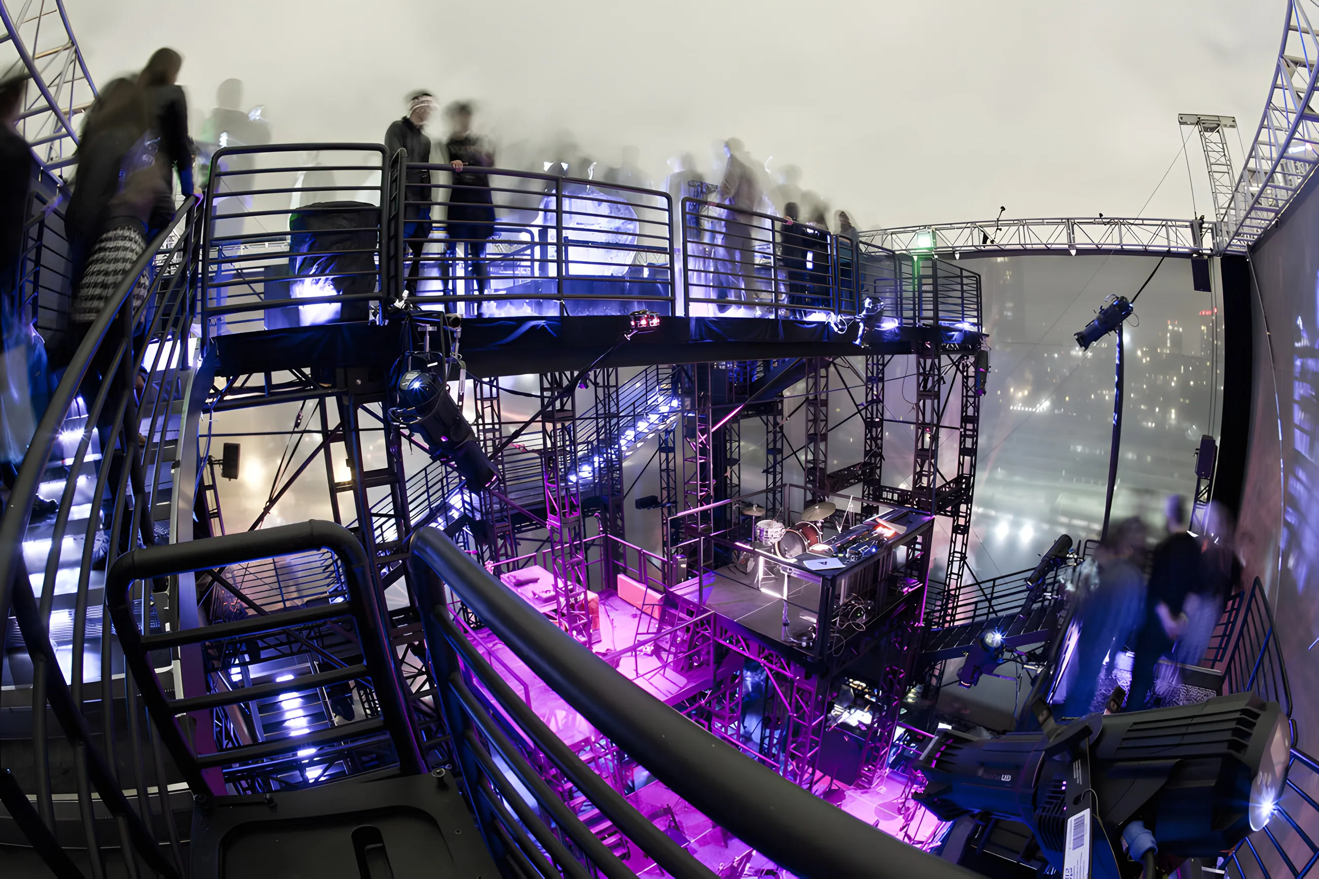 Fisheye view down through the scaffold interior, magenta uplighting, a drum kit and control desk on the lower deck