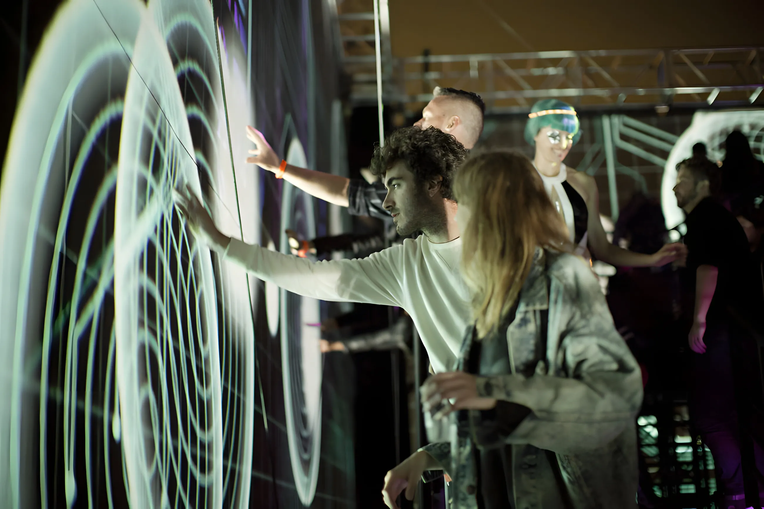 Visitors pressing hands against a screen of white concentric rings, one man reaching out in a pale sweatshirt