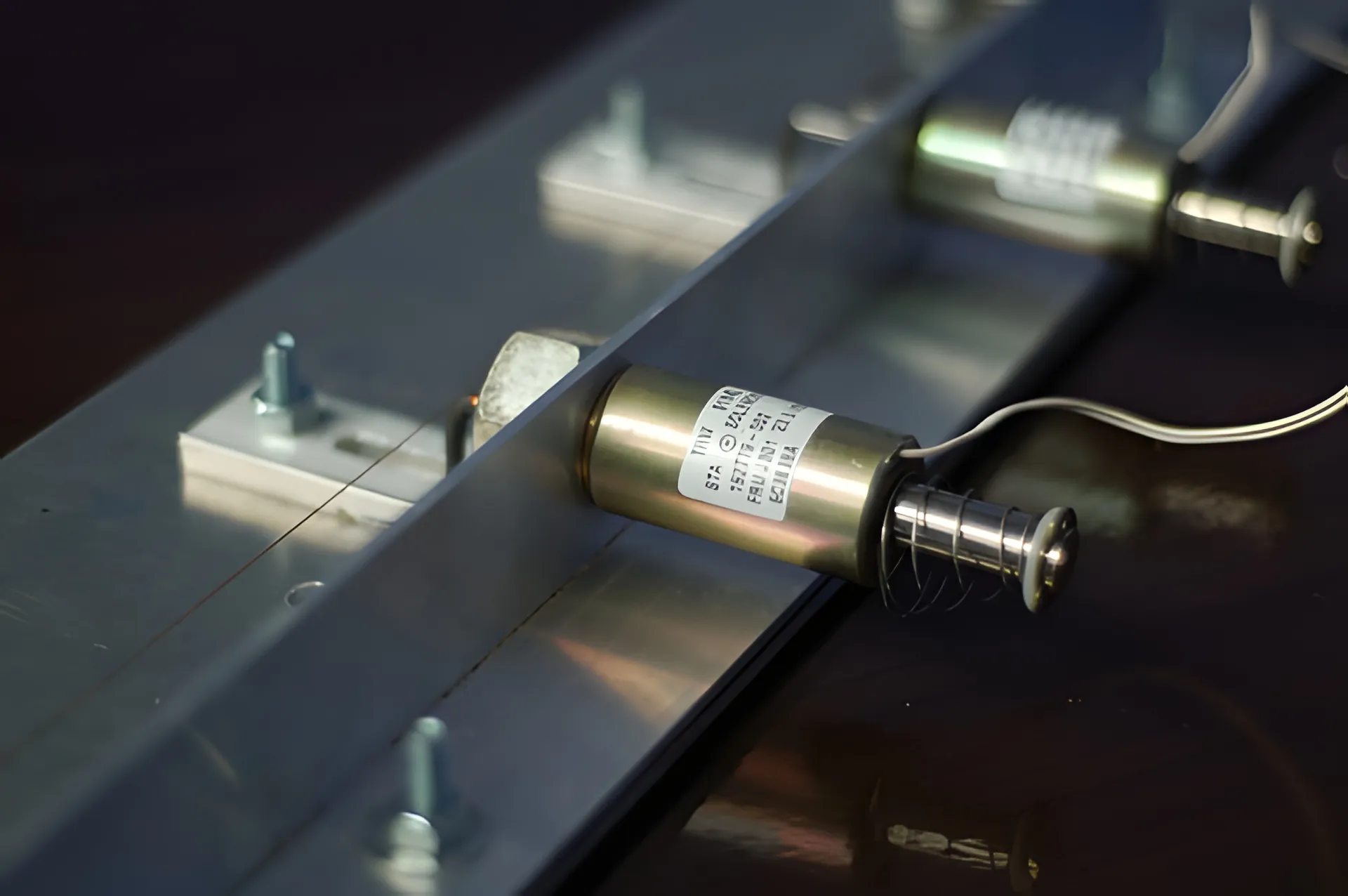 Close view of cylindrical push solenoids bolted along an aluminium rail, one with its coiled striker shaft extended